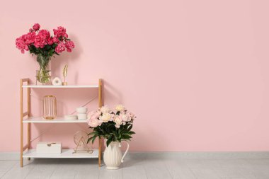 Odanın içindeki pembe duvarın yanında güzel şakayık çiçekleri olan raf ünitesi ve vazolar.