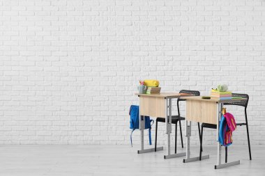 Okul sıraları ve beyaz tuğla duvarın yanında sırt çantaları.