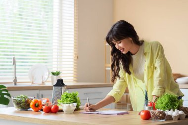 Evdeki masada yemek tarifi yazan genç bir kadın.