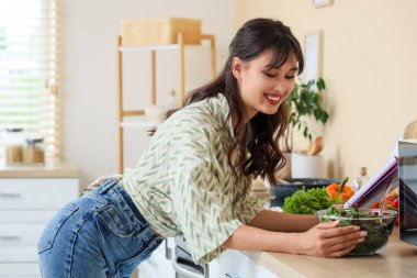 Mutfakta yemek tarifi kitabı ve sebze salatası olan genç bir kadın.