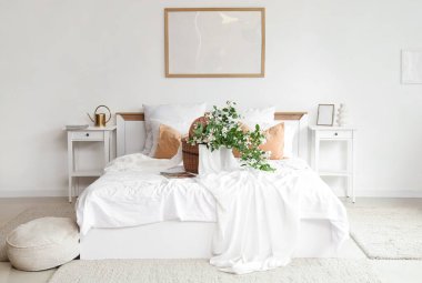 Konforlu yatak, komodinlerin yanında sepet ve yatak odasının içinde çiçek açan yasemin çiçekleri.