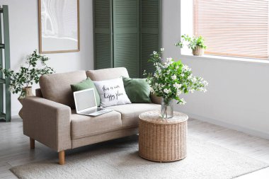 Kanepe, masa, modern dizüstü bilgisayar ve vazo. Oturma odasının içinde çiçek açan yasemin çiçekleri.