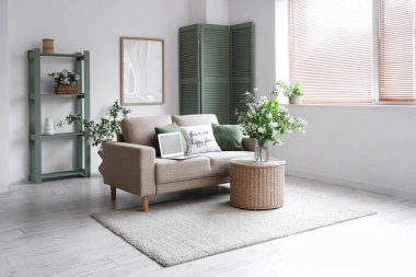 Kanepe, masa, modern dizüstü bilgisayar ve vazo. Oturma odasının içinde çiçek açan yasemin çiçekleri.