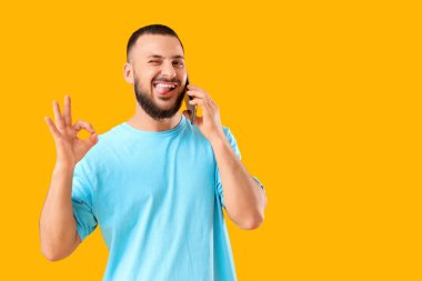 Yakışıklı genç adam telefonla konuşuyor ve sarı arka planda iyi bir hareket gösteriyor.
