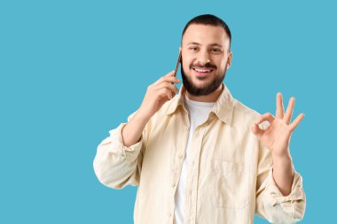 Yakışıklı genç adam cep telefonuyla konuşuyor ve mavi arka planda iyi bir hareket gösteriyor.