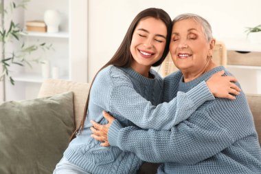 Mutlu genç bir kadın ve büyükannesi evde kanepede sarılıyorlar.