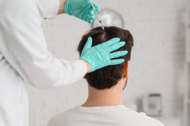 Doktor klinikte saç büyümesi için adama iğne yapıyor.
