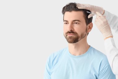 Doktor arka planda saç büyümesi için adama iğne yapıyor.