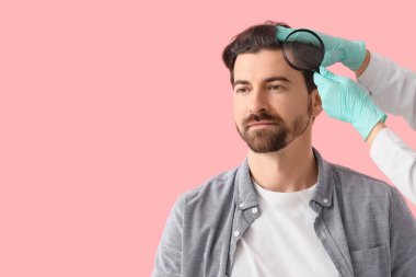 Pembe arka planda büyüteç kullanarak saç kaybı sorunu olan adamı muayene eden doktor.