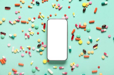 Cep telefonu ve turkuaz arka planda dağınık haplar.