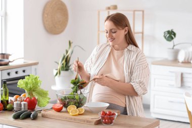 Genç hamile kadın mutfakta sebze salatası karıştırıyor.