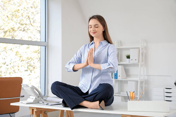 Young businesswoman meditating on desk in office