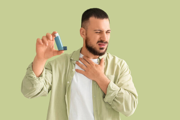 У молодого человека с ингалятором приступ астмы на зеленом фоне