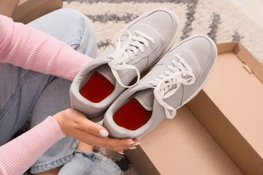 Gri spor ayakkabılarını evdeki karton kutuya koyan kadın, yakın plan.