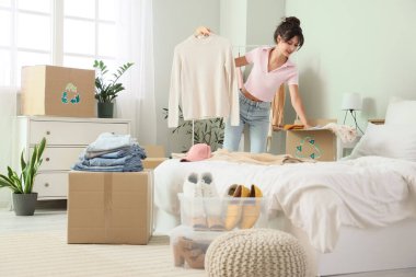 Yatak odasında geri dönüşüm için süveter paketleyen genç bir kadın.