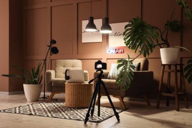 Podcaster 'ın stüdyosunun içinde koltuklar, bitkiler ve parlayan lambalar var.