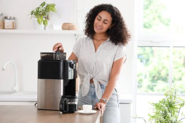 Genç Afro-Amerikalı kadın mutfakta kahve makinesi kullanıyor.