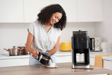 Genç Afro-Amerikalı kadın mutfakta fincana sıcak kahve dolduruyor.