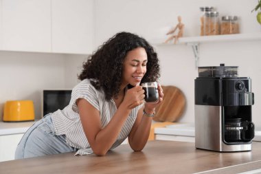 Genç Afro-Amerikalı kadın mutfakta kahve içiyor.