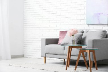 Oturma odasındaki kanepenin yanındaki masada pembe ortanca çiçekli vazo.