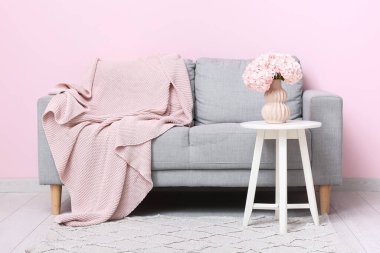 Oturma odasındaki kanepenin yanındaki masada pembe ortanca çiçekleri olan vazo.