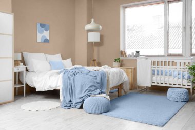 Büyük yataklı, bebek karyolası ve pencereli aydınlatma odasının içi.