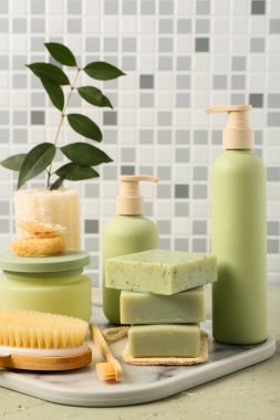 Farklı kozmetik ürünleri ve banyo malzemeleriyle dolu tepsi gri kiremit duvara karşı.