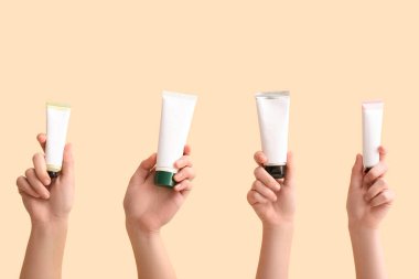 Bej arka planda farklı kozmetik kremlerden tüpler olan kadın elleri