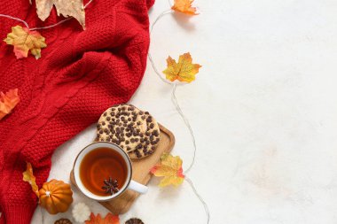 Bir fincan çay, kurabiye, şık bir süveter ve arka planda sonbahar yapraklarıyla kompozisyon