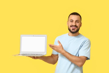 Sarı arka planda boş dizüstü bilgisayarı olan genç bir adam.