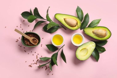 Taze avokado, bir kase yağ, keten tohumu ve pembe arka planda bitki dalları içeren kompozisyon