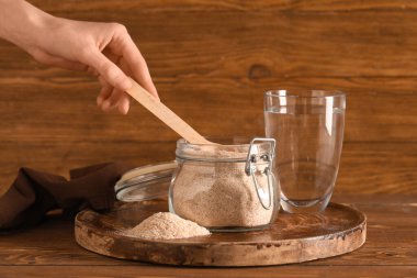 Kadın eli ve kavanozu ile psyllium kabuk tozu ile ahşap zemin üzerinde bir bardak su