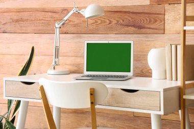 Odasında ahşap duvarın yanında dizüstü bilgisayarı olan modern işyeri.