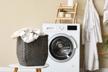 Banyoda bej duvarın yanında çamaşır sepeti olan modern çamaşır makinesi.