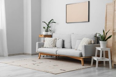 Kahve masalı kanepe, ev bitkileri ve oturma odasındaki gri duvarın yanındaki fotoğraf çerçevesi.