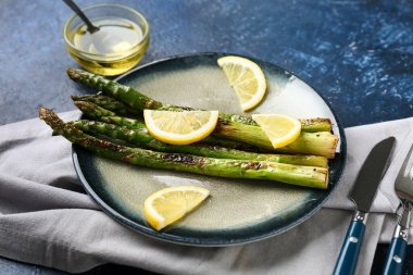 Kızarmış yeşil kuşkonmaz ve mavi arka planda limon dilimleri, yakın plan.