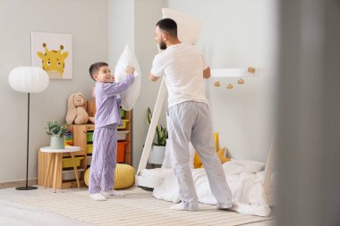 Pijamalı mutlu baba oğluyla yastık savaşı yapıyor.