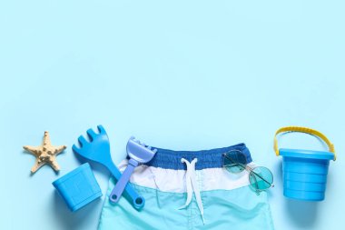 Mavi arka planda mayo, denizyıldızı, oyuncak tırmık ve kova kompozisyonu