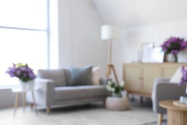 Kanepe ve vazolarda leylak çiçekleriyle aydınlık oturma odasının bulanık görüntüsü