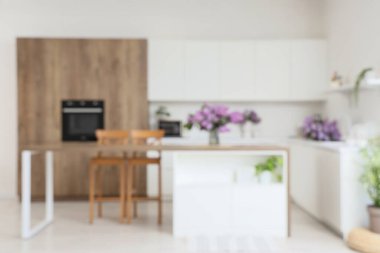 Masa, tezgah ve vazodaki leylak çiçekleriyle aydınlık mutfağın bulanık görüntüsü