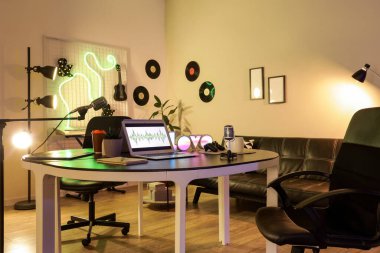Podcaster 'ın atölyesinin içinde çalışma yeri, kanepe ve parlayan lambalar var.