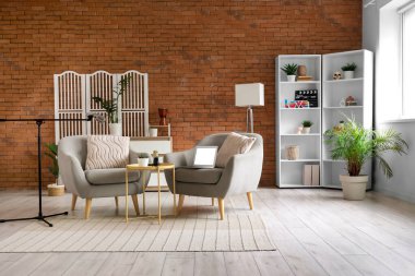 Podcaster 'ın stüdyosunun içinde koltuklar, katlanır ekran ve raf ünitesi