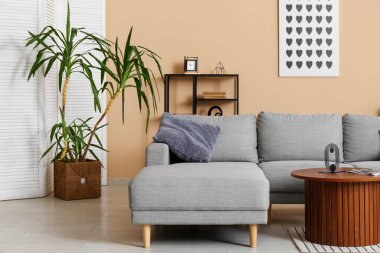 Oturma odasının iç tarafındaki bej duvarın yanında rahat bir kanepe ve masa var.