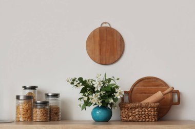 Mutfaktaki masada çiçek açan yasemin çiçekli kavanozlar, çatal bıçaklar ve vazolar, yakın plan.