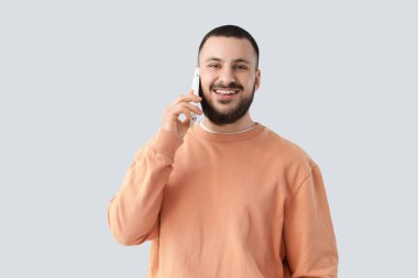 Güzel gülüşlü genç adam arka planda cep telefonuyla konuşuyor.