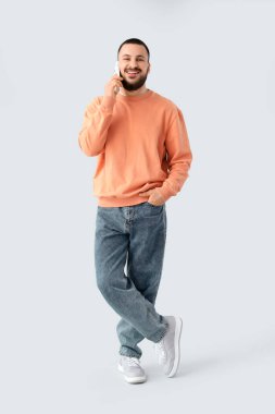 Güzel gülüşlü genç adam arka planda cep telefonuyla konuşuyor.