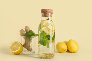 Sarı arka planda zencefil ve fesleğen yapraklı bir şişe taze limon.