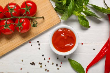 Bir kase lezzetli ketçap ve beyaz ahşap arka planda farklı malzemeler.