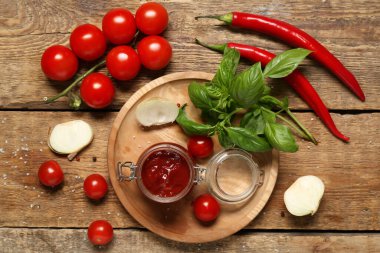 Lezzetli ketçap kavanozu ve ahşap arka planda farklı malzemeler.