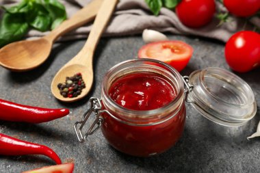 Lezzetli ketçap kavanozu ve koyu arkaplanda farklı malzemeler, yakın plan.